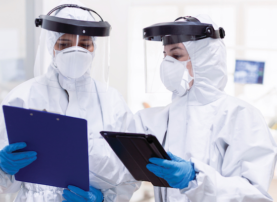 two women in protective suites looking at clipboards in a lab